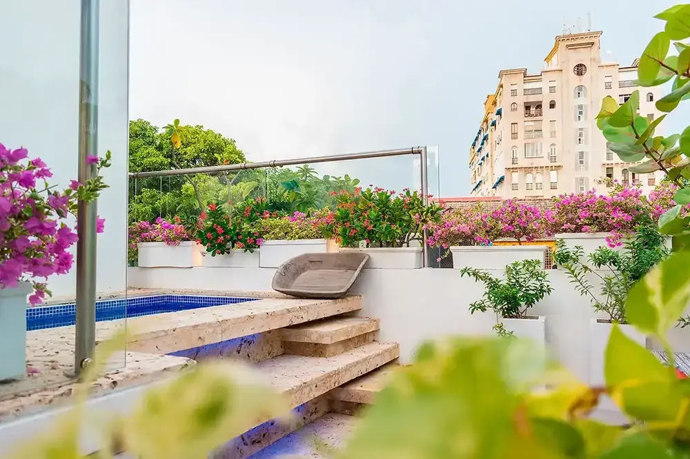 The courtyard plunge pool at Santo Toribio, tiled in turquoise and olive mosaic, running beside a wall of vertical planting with palms and red euphorbia, wrought-iron table and chairs on the stone paving beyond